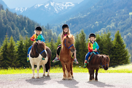 在阿尔卑斯山上骑小马的孩子们。家庭春天假期在马牧场在奥地利, Tirol。孩子们骑着马。照顾动物的孩子孩子和宠物。小女孩和男孩在马鞍在小马.