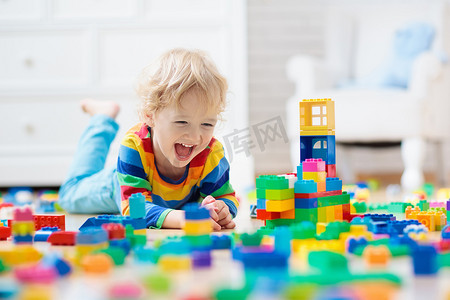 游戏摄影照片_孩子们玩五颜六色的玩具块.小男孩在家里或托儿所建塔。幼儿教育玩具。婴儿或幼儿的建筑块。幼稚园游戏室的烂摊子.