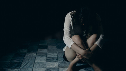 person摄影照片_Young person woman sad, stress and loneliness sitting in dark room, Unhappy and crying teenage girl from domestic violence, An adult female expresses feelings of despair, anxiety from harassment.