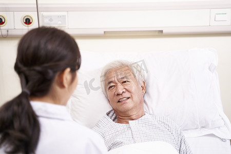 亚洲老人躺在床上与年轻的女医生交谈