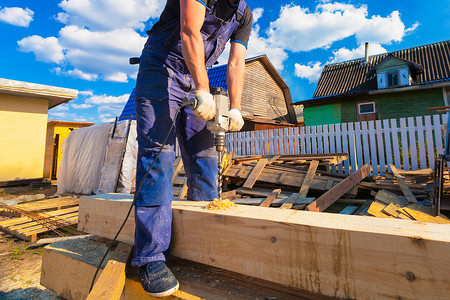 木匠 (工人) 用大的专业工具 (电钻) 在改建、翻新、扩建、修复、改建和施工中钻木梁 