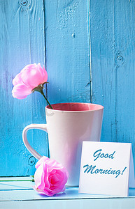 杯子，粉红玫瑰的蓝色木背景与早上好文本