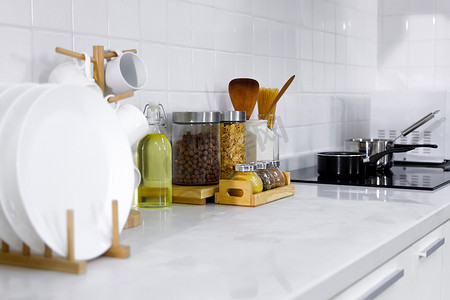 厨房里的现代白色柜台，有盘子、器皿、麦片、集装箱和炉灶中的调味品.