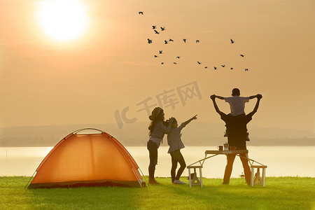 快乐的家庭露营附近的湖与日落或日出 