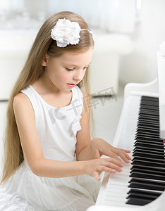 幼小的孩子弹钢琴的白色连衣裙的肖像