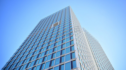 close摄影照片_Commercial building close up in blue tone. Gigantic skyscraper from below. Architecture details of modern building amd glass facade. Business background on a beautiful sunny day. 