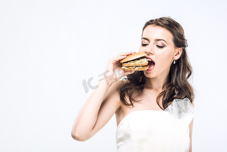 饥饿的年轻新娘穿着婚纱吃着白色的大汉堡