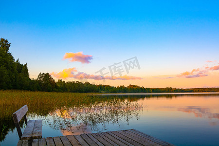 塞利格湖的夏日之夜。美丽的夕阳天空映照在水面上。前景的簧片丛。远岸是一片森林。休息和放松.