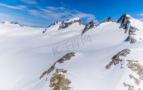 An aerial view of mountain peaks protruding through snow above the Denver glacier close to Skagway, Alaska in summertime