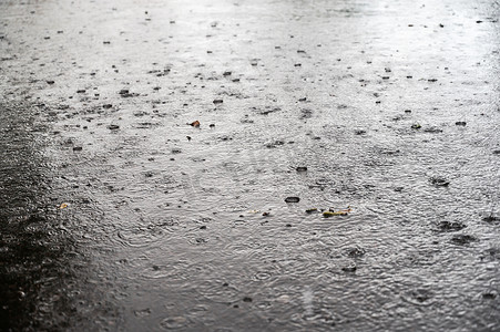 下暴雨摄影照片_城市街道上夏季暴雨的纹理。在城市的一条柏油路上，下着暴雨。夏天的雷雨掉下大雨滴。有选择的重点。运动模糊。噪音、颗粒效应.