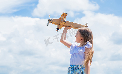 小孩梦想摄影照片_坐飞机旅行。继续做梦小孩玩木制玩具飞机。学习地理。关于旅行的梦想。暑假的故事。小女孩拿着木制的飞机。想象力