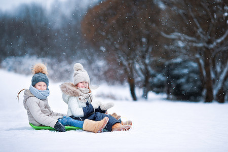 可爱的小女孩享受驾雪橇。滑雪橇的孩子。在雪中，孩子们在户外玩。在圣诞前夕户外家庭度假