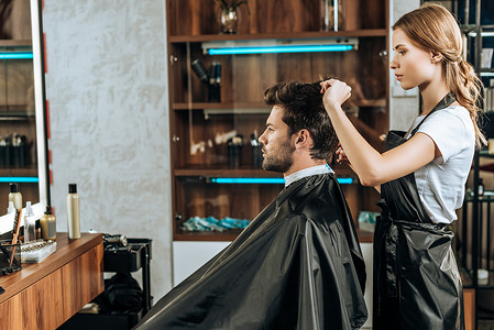 剪头发摄影照片_发型师在美容院剪头发英俊的年轻人的侧视图  