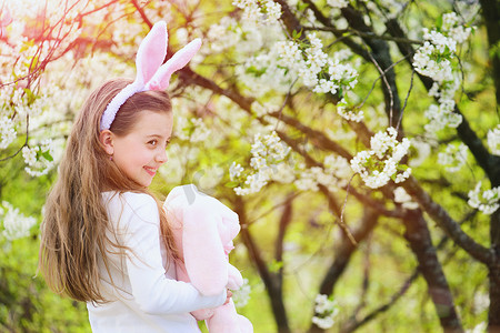 快乐的女孩，抱着粉红的兔子在开着花的花园里