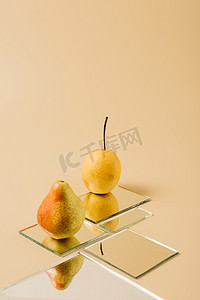 两个黄梨反射在米色桌子上的镜子上 