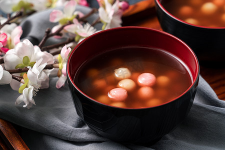饺子汤圆摄影照片_用红白相间的汤圆（汤圆，糯米饺子球）和甜糖浆汤盛在蓝色桌旁的碗里，准备过冬.