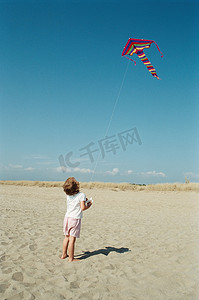 政府蓝背景摄影照片_在海滩上放风筝的孩子