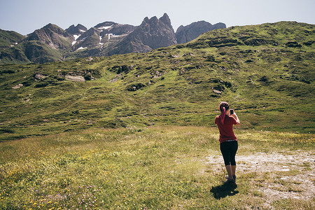 十几岁的女孩用智能手机拍摄山脉的背影贝林佐纳特森瑞士