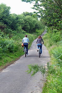 两个年轻的成年姐妹沿着乡间小路骑自行车的后景