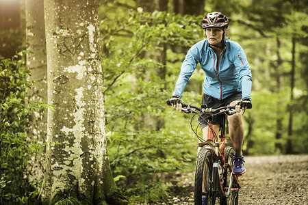 成熟的女性山地自行车手在森林小径上骑自行车