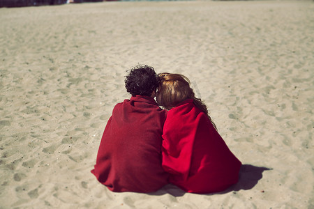 海滩上裹着毯子的浪漫情侣的背影