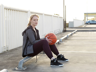 运动裤女摄影照片_年轻的女篮球运动员坐在停车场