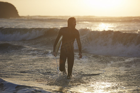 在英国德文郡的海上年轻的男性冲浪者背着冲浪板的剪影
