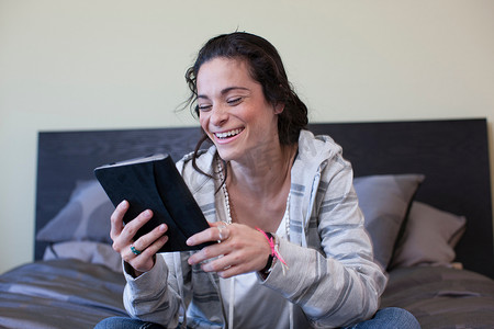 年轻女子坐在床上看电子书微笑着