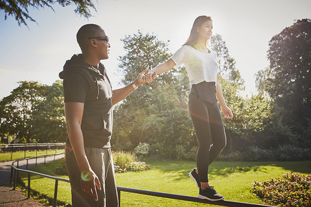 男运动裤摄影照片_一名女子与私人教练手牵手走在公园栅栏上