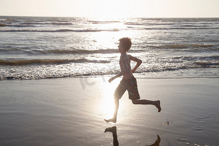 在阳光下奔跑摄影照片_男孩在阳光下沿着海滩奔跑
