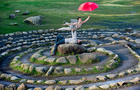 中年舞者打着红伞在石圈里表演
