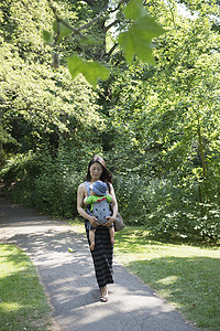 漫步摄影照片_穿着婴儿吊带的成熟母子在公园里散步