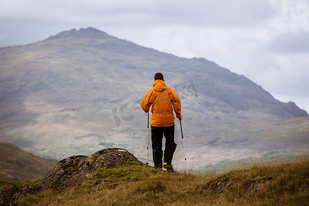 年轻男性徒步旅行者向外眺望英国坎布里亚郡湖区山区的背影