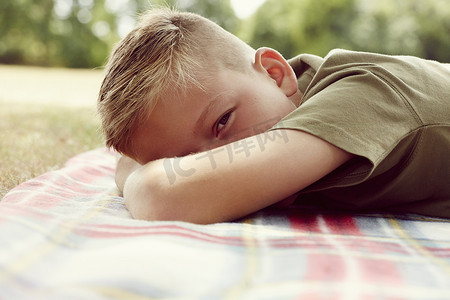 男孩躺在野餐毯子上的表面平面图脸被遮挡着看着相机