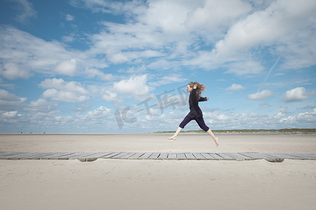 张开双臂得人摄影照片_德国石勒苏益格·荷尔斯泰因圣彼得·奥丁斯在木板路上跳跃的女人