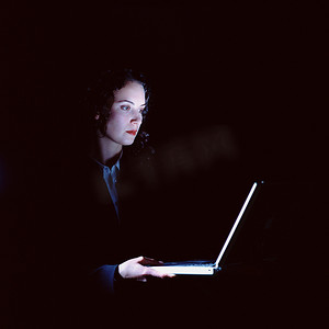 女商人在黑暗中拿着笔记本电脑