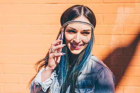 手机文化墙摄影照片_染蓝头发的年轻女子在橙色墙前用智能手机聊天