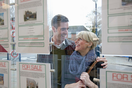 橱窗广告摄影照片_一对夫妇看着房地产中介的橱窗
