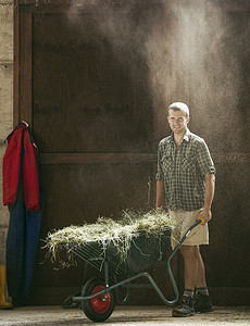 在尘土飞扬的农场谷仓里推着手推车的年轻农场工人肖像