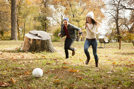一对年轻夫妇在秋季公园追逐足球