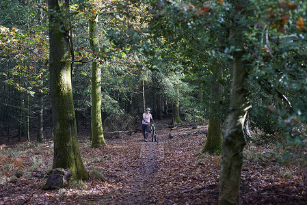 英国布里斯托尔迪恩森林女山地自行车手推着山地车穿过秋天的树叶
