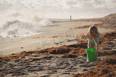 美国佛罗里达州朱庇特岛吹石保护区女孩在多风的海滩上玩玩具桶