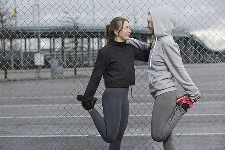 运动裤女摄影照片_两位女跑步者朋友在铁丝网上伸腿