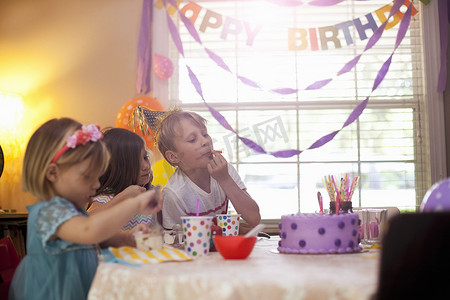 三个孩子坐在桌子边吃紫色生日蛋糕