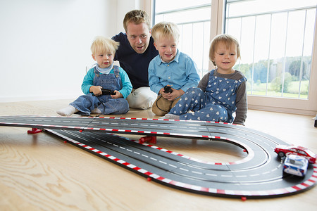 一名中年男子和三名儿童在客厅地板上玩玩具赛车