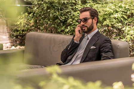迪拜酒店摄影照片_阿联酋迪拜一名商人在酒店花园沙发上用智能手机交谈