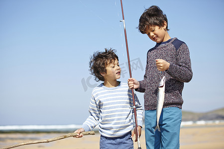 两个小男孩站在一起手里拿着鱼竿和鱼
