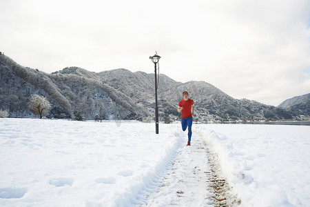 男运动裤摄影照片_日本富士山川口湖一名男子沿着积雪覆盖的赛道跑步