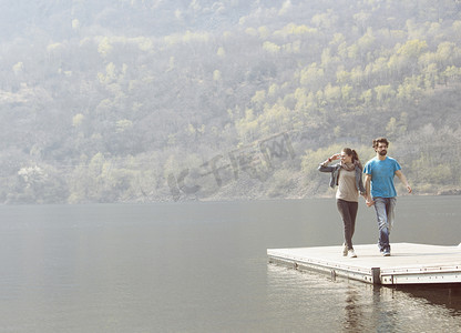 漫步摄影照片_一对年轻夫妇在意大利皮埃蒙特韦尔巴尼亚的梅尔戈佐湖码头上散步