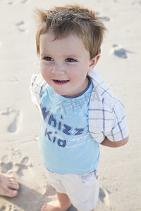 微笑标语摄影照片_海滩上的男孩双手放在身后微笑着看着别处